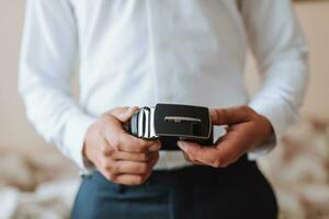un hombre sostiene un negro cinturón en su manos, de cerca foto. el novio es preparando para el Boda ceremonia foto