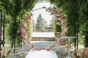 The wedding arch in the park is made of fresh flowers and dry reeds. Outdoor wedding ceremony in nature in a green corridor. White chairs for the ceremony photo