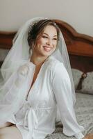 Beautiful young bride in white petticoat and tiara sitting posing on bed in her bedroom. Final preparations for the wedding. The bride is waiting for the groom. Morning, bride. photo