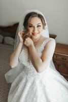 Portrait of the bride. The bride is dressed in an elegant dress, posing by the window wearing earrings. Tiara and jewelry. Open bust. Morning of the bride photo