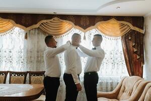 Boda fotografía. amigos ayuda el novio obtener vestido. del novio Mañana. estilo. moda. el mismo ropa foto