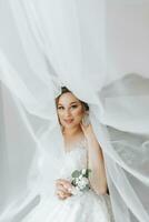 Portrait of the bride. The bride in a veil, posing with a boutonniere, on a white background. Beautiful hair and makeup. Open bust on the dress. Diadem with crystals photo