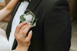 hermosa novia poniendo en elegante sencillo flor en el ojal con rosas en novio negro traje. Boda Mañana preparativos foto