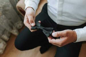 un hombre sostiene un negro arco Corbata en su manos, de cerca foto. el novio es preparando para el Boda ceremonia foto