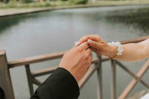 el novio suavemente sostiene el de la novia mano en contra el antecedentes de el lago. de cerca foto