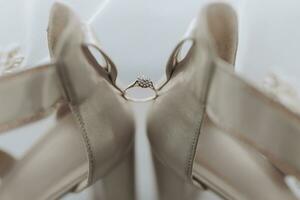 desnudo elegante zapatos. un diamante compromiso anillo se sienta Entre un par de clásico desnudo nupcial zapatos. moda. estilo. Boda foto