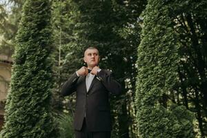 portrait of the groom in a classic suit against a background of green trees. A young man. Style. Fashion photo