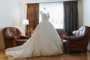 un Exquisito Boda vestir con un largo tren, hecho a mano, en un maniquí en el de la novia habitación. Boda detalles. foto