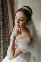 Preparation for the wedding. Beautiful young bride in white luxurious wedding dress, tiara on head, long veil in royal hotel room. Luxury smiling model photo