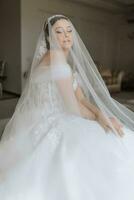 preparación para el boda. hermosa joven novia en blanco lujoso Boda vestido, tiara en cabeza, largo velo en real hotel habitación. lujo sonriente modelo foto