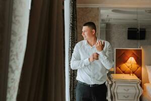 A stylish groom is preparing for the wedding ceremony. Groom's morning. Businessman in white shirt in hotel, male hands close-up, groom getting ready in morning before wedding ceremony photo