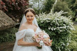 Portrait of a beautiful bride in a white wedding dress with a long train with a modern hairstyle and a veil walking in the garden. Wedding concept photo