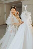 a beautiful girl with a wedding hairstyle in a transparent robe is preparing for a wedding in a hotel with a royal interior. The bride poses next to her wedding dress on a mannequin photo