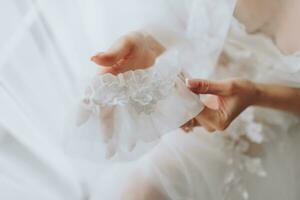 the bride with a French manicure holds a white garter in her hands. Close-up photo