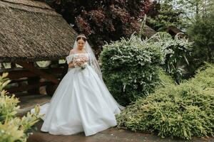 Portrait of a beautiful bride in a white wedding dress with a long train with a modern hairstyle and a veil walking in the garden. Wedding concept photo