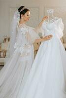 a beautiful girl with a wedding hairstyle in a transparent robe is preparing for a wedding in a hotel with a royal interior. The bride poses next to her wedding dress on a mannequin photo