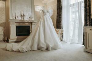 Royal living room interior with a fireplace and a large window, a wedding dress on a mannequin in the middle of the room, prepared for the ceremony photo