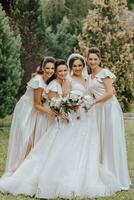 A group of beautiful girls with a bride in identical dresses are smiling, celebrating and having fun together against the background of nature and tall trees. Girls party photo