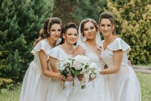 A group of beautiful girls with a bride in identical dresses are smiling, celebrating and having fun together against the background of nature and tall trees. Girls party photo