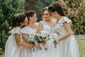 A group of beautiful girls with a bride in identical dresses are smiling, celebrating and having fun together against the background of nature and tall trees. Girls party photo
