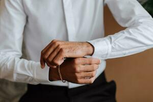A stylish groom is preparing for the wedding ceremony. Groom's morning. Businessman in white shirt in hotel, male hands close-up, groom getting ready in morning before wedding ceremony photo