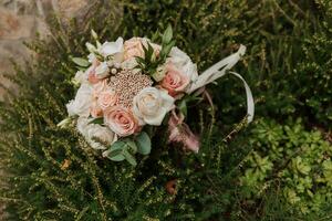 wedding bouquet of pink roses, feathers and dry flowers on the stones in the park photo