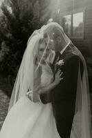 gorgeous happy luxurious brunette bride and elegant stylish groom stand under a veil and embrace tenderly photo