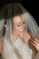 Happy and beautiful bride under a veil close-up. bride with professional makeup and hairstyle on a dark background. photo