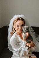 a young, elegant girl in the image of a bride with a beautiful veil on her head, holding her domestic cat in her arms Scottish Fold photo