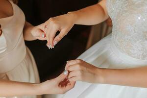 Morning preparation of the bride. Close-up of bridesmaid's hands holding hands of bride. The bride in a white wedding dress is standing in the room. photo