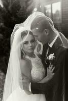 gorgeous happy luxurious brunette bride and elegant stylish groom stand under a veil and embrace tenderly photo