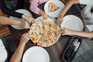 An overhead shot of a group of unidentified people grabbing a slice of Hawaiian pizza photo