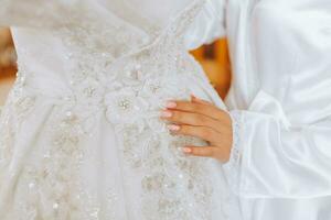 happy brunette bride in white satin dress with long veil, professional make-up and hairstyle. The bride touches her wedding dress photo