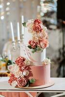 A delicious wedding. Pink three-tiered cake decorated with flowers. Candy bar for a banquet. Celebration concept. Fashionable desserts. Table with sweets, candies. Fruits photo