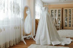 white wedding dress with long train near mirror in room with home interior photo