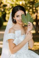 Happy bride and groom after wedding ceremony. Long veil. Chic white dress with open shoulders. A bouquet of orchids. During sunset photo