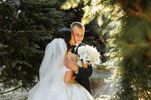 Happy bride and groom are walking in the park after the wedding ceremony. Long veil. Chic white dress with open shoulders. A bouquet of orchids. During sunset photo