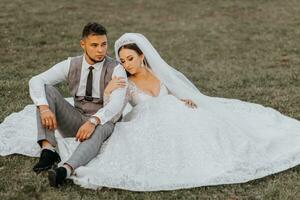 Fashionable groom and cute brunette bride in white dress with crown, hugging, laughing in park, garden, outdoors. Wedding photography, portrait of smiling newlyweds. photo