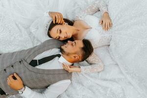 Fashionable groom and cute brunette bride in white dress with crown, hugging, laughing in park, garden, outdoors. Wedding photography, portrait of smiling newlyweds. photo