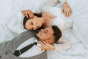 de moda novio y linda morena novia en blanco vestir con corona, abrazando, riendo en parque, jardín, al aire libre. Boda fotografía, retrato de sonriente recién casados. foto