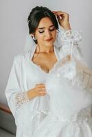 Portrait of a girl in a morning robe. Happy bride with professional make-up and long veil posing for photographer. The bride is preparing for the wedding photo