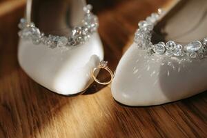 Beige elegant shoes. A diamond engagement ring sits between a pair of classic wedding shoes. Fashion. Style. Wedding photo