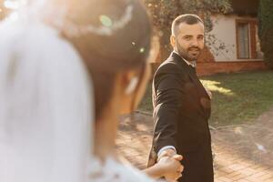 The groom leads the bride by the hand during sunset. photo