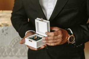 A stylish groom is preparing for the wedding ceremony in the morning. Groom's morning. A man in a classic suit and a bow tie. Young and handsome groom with wedding rings in his hands photo