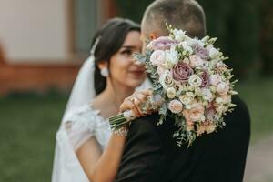 Portrait of a happy newlywed wife and husband hugging outdoors and enjoying a wedding bouquet of white roses. Sincere feelings of two young people. The concept of true love. photo