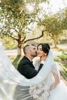 retrato de el novia y novio besos en contra el antecedentes de el otoño Dom de verde arboles en el jardín o parque. un increíblemente hermosa novia. elegante novio con un barba foto