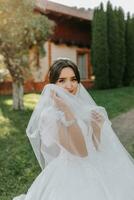 hermosa novia en un de moda Boda vestir en un natural antecedentes en el parque. un maravilloso joven novia es increíblemente contento. contento niña en su Boda día foto