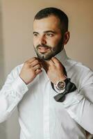 Young groom wearing bow tie, hands close-up, looking at camera. The man is wearing a shirt. The groom is preparing for the wedding. photo