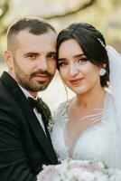 Portrait of a happy newlywed wife and husband hugging outdoors and enjoying a wedding bouquet of white roses. Sincere feelings of two young people. The concept of true love. photo