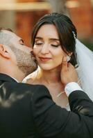 portrait of the bride and groom kissing against the background of the autumn sun of green trees in the garden or park. An incredibly beautiful bride. Stylish groom with a beard photo